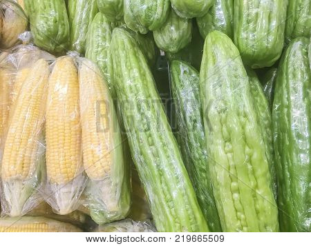 Closeup surface pile of fresh green bitter cucumber and corn in plastic rap for sell textured background