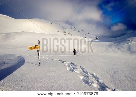 Early morning sun breaking through over a fantastic mountain landscape covered with a lot fresh snow. There is a snowshoe hiker following a new trail through this majestic landscape