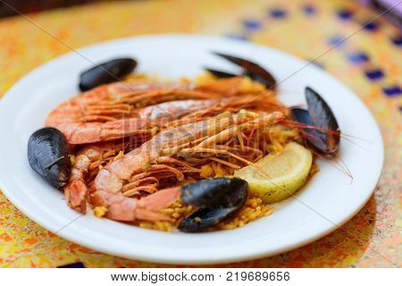 Royal Paella. Tasty Rice with king prawns, mussels and lemon on white plate