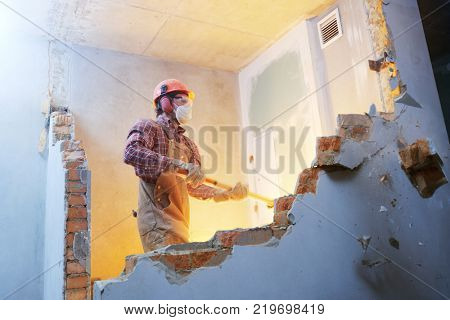 worker with sledgehammer at indoor wall destroying