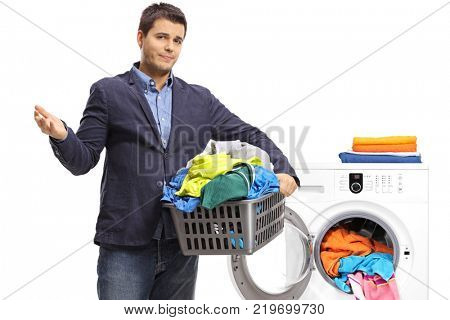 Unhappy elegant guy holding a laundry basket filled with clothes in front of a washing machine isolated on white background
