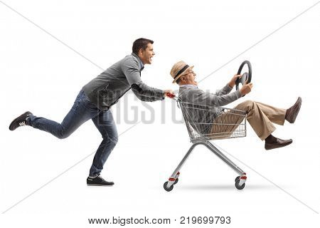 Young man pushing a shopping cart with a mature man holding a steering wheel riding inside isolated on white background