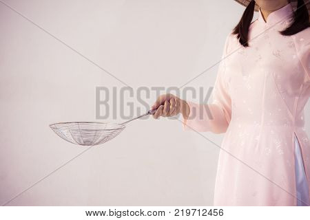 beautiful woman in pink dress and vietnam hat holding cooking utensils.