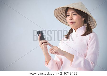 beautiful woman in pink dress and vietnam hat holding smartphone.