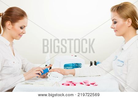 Relaxing time and wellness day concept. Blonde elegant woman visiting professional manicurist salon. Beautician makes perfect nails to client.