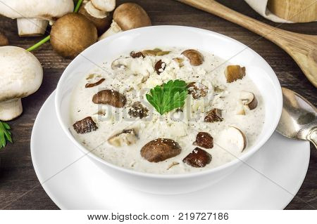 A closeup photo of a plate of a mushroom cream soup with champignons, cremini, fresh parsley, and pepper, on a dark rustic background