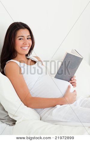 หญิงตั้งครรภ์ที่น่าสนใจที่อ่านหนังสือในขณะที่นอนอยู่บนเตียง
