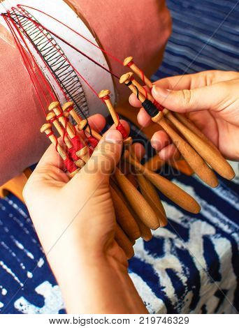Making bobbin lace in traditional way. Detail on hands holding wooden bobbins with wound thread. Pillow lace.
