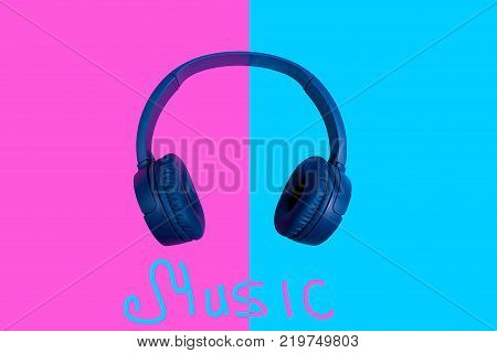 Top view on wireless headphones on vivid two colored background with music word written. Flat minimal style. Design and colors