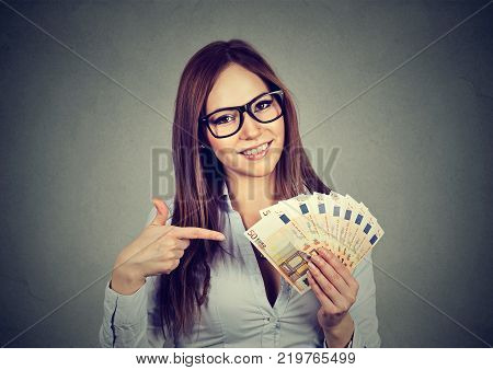 Happy successful young business woman holding money euro bills in hand isolated on gray background. Positive emotion facial expression. Financial reward concept