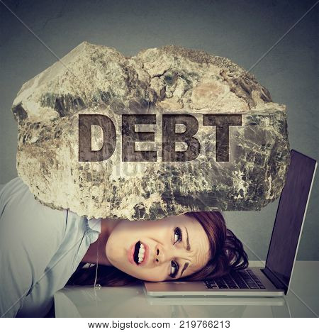 Young desperate business woman with her head squeezed between laptop computer and a rock. Student university education loan debt concept