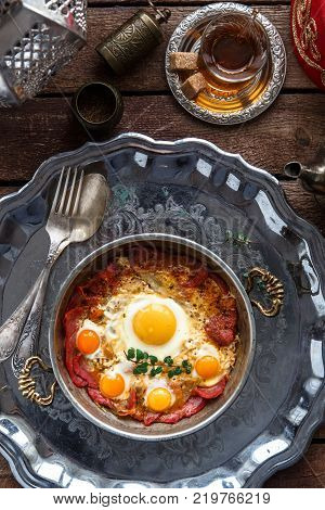 Fried egg with cured meat, traditional turkish breakfast, served in metal dishware, rustic.