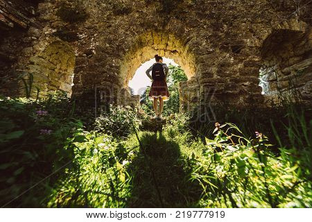 Young woman traveler in skirt standing in ancient temple with green plants  frame,looking around,summer travel vacations
