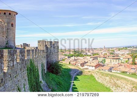 City view Carcasoone village from the Carcassone castle a fortified town in south of French. Big wall 's brick of castle and tower is install higher than village see all over orange roof top with background blue sky and white cloud.
