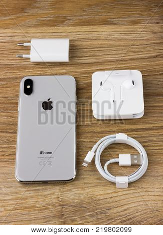 Rostov-on-Don, Russia - December 12, 2017: Iphone 10 rests on a wooden table next to the cable, charger and headset earpods.