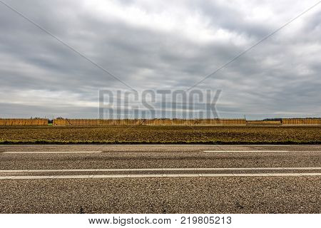 Asphalt road in front of a field with a long wall of hay piles