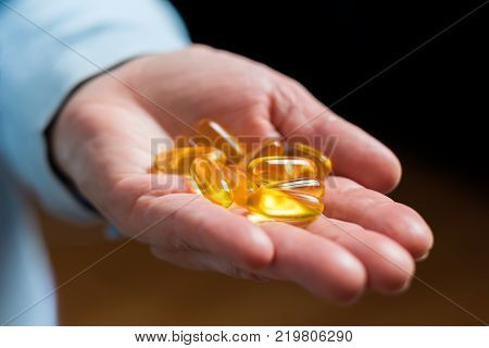 White medication capsules of glucosamine healthy supplement pills in woman palm hand demonstrate one pill.