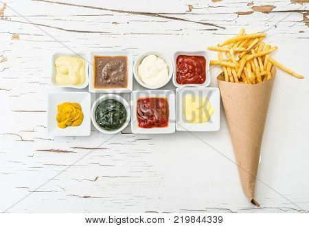 French fries on a piece of crafted paper with different sauces in white sausers on the white wooden background with cracking paint