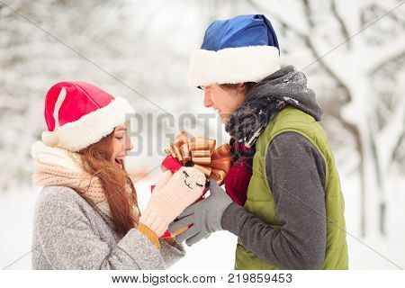 An attractive lady in a funny hat takes a present. She definetely likes it.