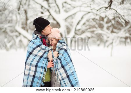 Young couple stays close to each other having checkered plaid on their shoulders.