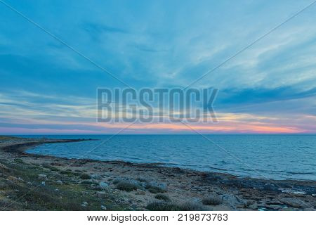 View over the seafront of the city Paphos in Cyrpus. Palm silhouettes, boats in the water and golden sunset over the sea with dramatic cloudy sky.
