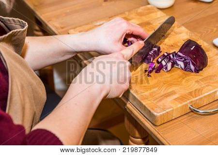 Female hands chopping red cabbage with knife on wooden board.