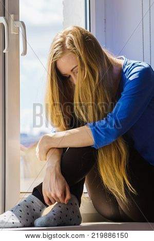 People and solitude concept. Alone sad young woman long hair teen girl sitting on window sill lost in thought urban city in the background