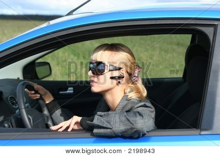 Young Blond Woman In A Blue Car In Sun-Glasses With Hands Free