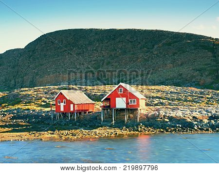 Rural Norwegian landscape traditional red and white wooden house on rocky island. Suny spring day with smooth water level in bay.