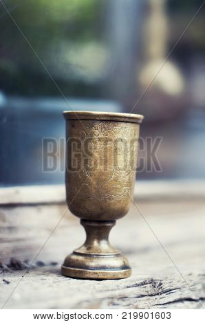 An ancient brass wineglass with an ornament from India stands on a wooden half shell. Selective focus.