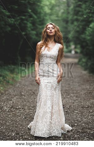 Beautiful bride in elegant white dress holding bouquet posing in park.