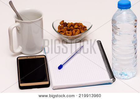mobile phone and notebook on the desk with bowl of huzelnuts bottle of water and the cup of coffee for keeping energy while working