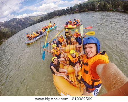 mountain Altai RUSSIA - July 16 2017: man in helmet holds action camera and makes selfie on background of friends with oars rafting