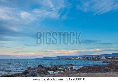 View over the seafront of the city Paphos in Cyrpus. Palm silhouettes, boats in the water and golden sunset over the sea with dramatic cloudy sky.