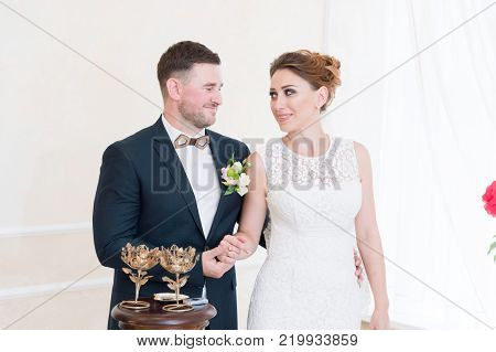 A beautiful happy couple in the registry office performs a wedding ritual with candle lighting. The concept of a happy marriage and marriage procession in the registry office.