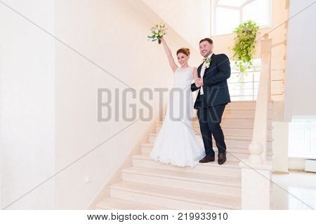 A couple of newlyweds go down the stairs in the registry office and greets those who meet them with smiles and gestures. The concept of marriage in the registry office