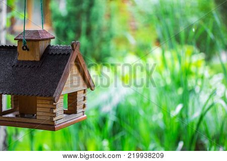 A feeder for birds made in a form of a house in a garden.