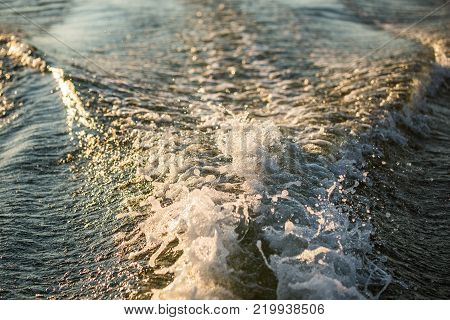 Close-up water surface behind of fast moving motor boat, evening time.
