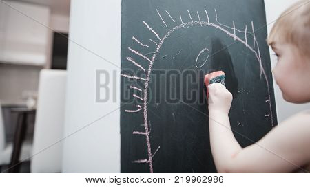 Cute little girl drawing on blackboard. Toddler girl having fun outdoors, holding chalk and drawing.