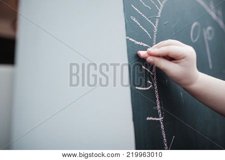 Cute little girl drawing on blackboard. Toddler girl having fun outdoors, holding chalk and drawing.