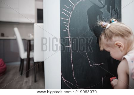 Cute little girl drawing on blackboard. Toddler girl having fun outdoors, holding chalk and drawing.