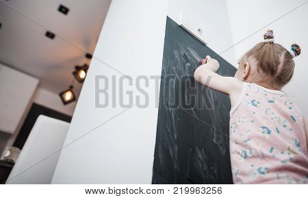 Cute little girl drawing on blackboard. Toddler girl having fun outdoors, holding chalk and drawing.