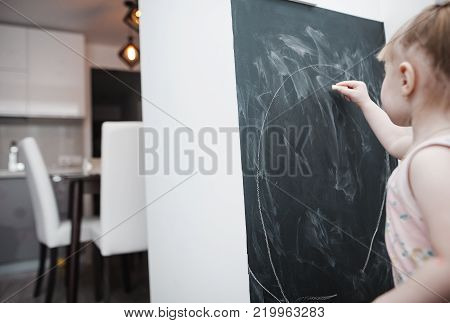 Cute little girl drawing on blackboard. Toddler girl having fun outdoors, holding chalk and drawing.