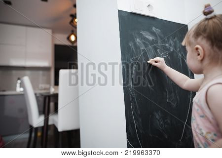 Cute little girl drawing on blackboard. Toddler girl having fun outdoors, holding chalk and drawing.