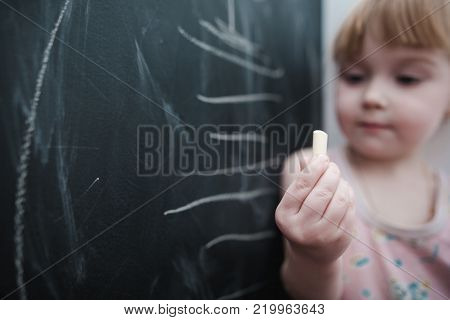 Cute little girl drawing on blackboard. Toddler girl having fun outdoors, holding chalk and drawing.