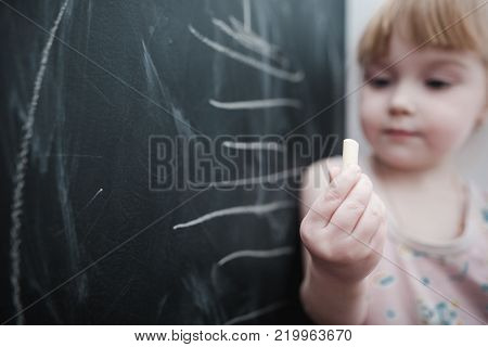 Cute little girl drawing on blackboard. Toddler girl having fun outdoors, holding chalk and drawing.