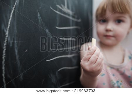 Cute little girl drawing on blackboard. Toddler girl having fun outdoors, holding chalk and drawing.