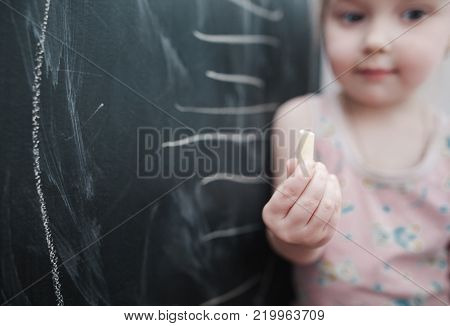 Cute little girl drawing on blackboard. Toddler girl having fun outdoors, holding chalk and drawing.