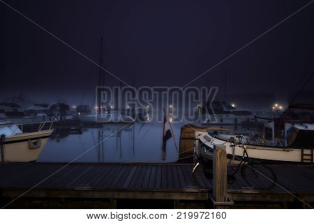 Yachts and sailboats docked at a platform in a calm and nightly city marina.