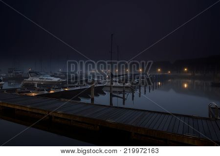 Yachts, small motorboats and sailboats docked at a platform in a calm and nightly city marina.